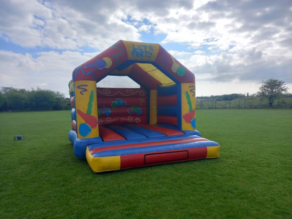 A colorful inflatable bouncy castle with the text 'LET'S PARTY' on the front, featuring various playful designs.