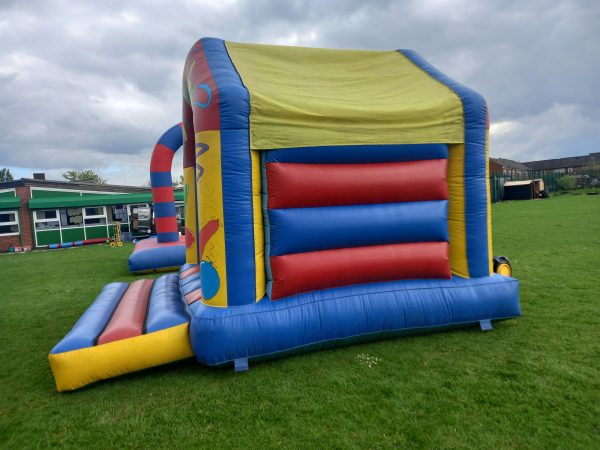 Colorful inflatable bounce house with a slide, featuring red, blue, and yellow sections.
