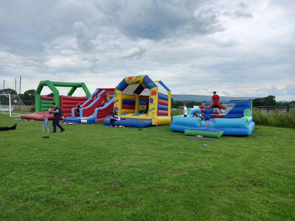 Multiple inflatable bounce houses and slides set up on grass, with children playing around them.