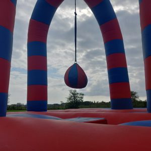 Inflatable battle zone with red and blue striped arches and a hanging ball in the center.