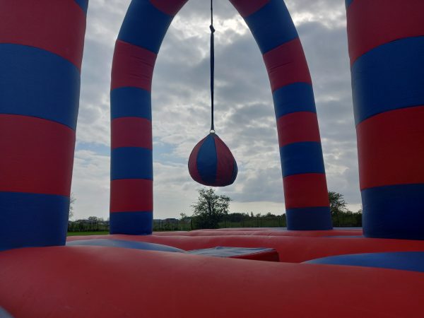 Inflatable battle zone with red and blue striped arches and a hanging ball in the center.