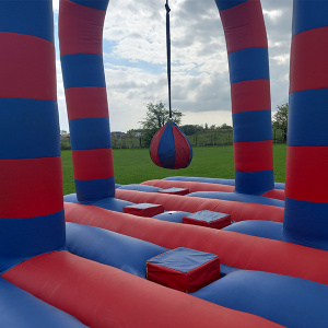 Inflatable battle zone featuring red and blue striped pillars and a hanging ball in the center.
