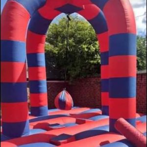 Inflatable bounce house featuring red and blue stripes with a hanging wrecking ball in the center.