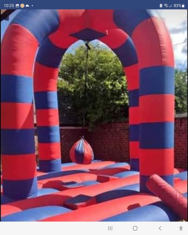 Inflatable bounce house featuring red and blue stripes with a hanging wrecking ball in the center.