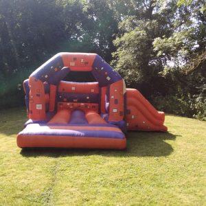 Inflatable bounce house with a slide, featuring a colorful design in orange and blue.
