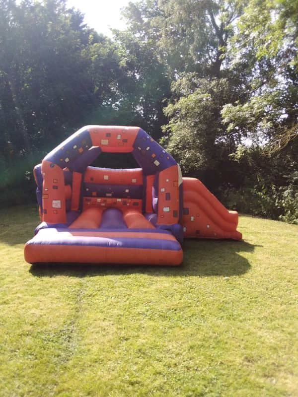 Inflatable bounce house with a slide, featuring a colorful design in orange and blue.