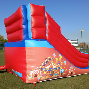 Red and blue inflatable slide with circus-themed graphics featuring a carousel and cartoon characters.