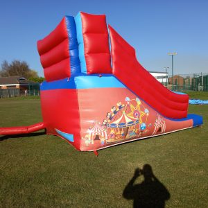 Red and blue inflatable circus slide with decorative graphics on the side.