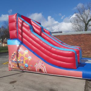Inflatable circus-themed slide with red and blue colors and carnival graphics.