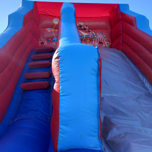 Circus-themed inflatable slide with red and blue colors and steps leading up the side.