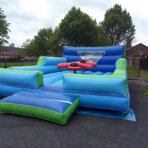 Inflatable gladiator arena with blue and green sections and a central platform for competition.
