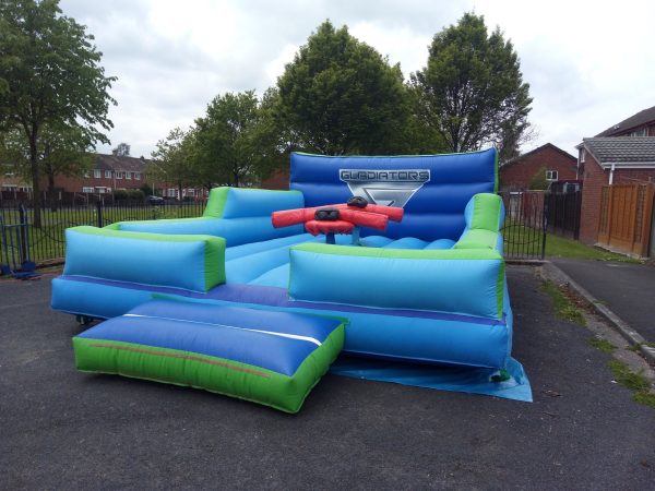 Inflatable gladiator arena with blue and green sections and a central platform for competition.