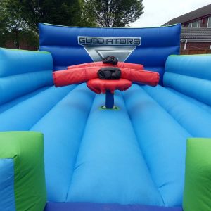 Inflatable Gladiator arena with blue and green sections and red padded equipment in the center.