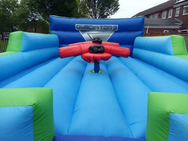Inflatable Gladiator arena with blue and green sections and red padded equipment in the center.