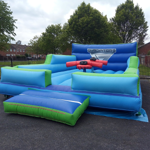 Inflatable gladiator arena featuring blue and green sections with a central platform and red inflatable weapons.