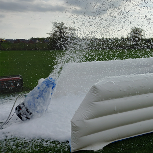 Foam cannon spraying foam in an outdoor setting with an inflatable structure.
