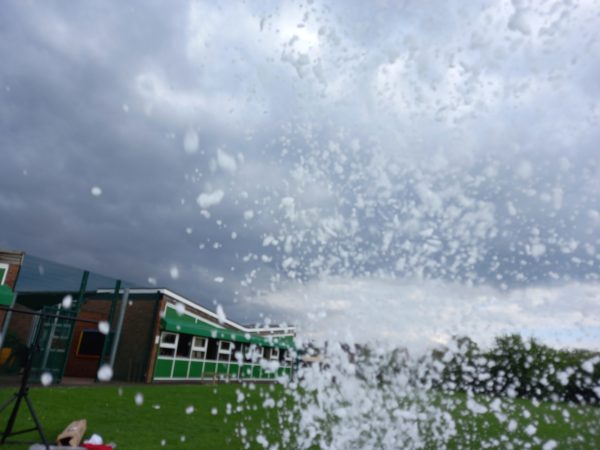 Foam being ejected from a foam cannon during an outdoor event with cloudy skies.