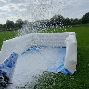 Inflatable foam cannon releasing foam in an outdoor setting on grass.