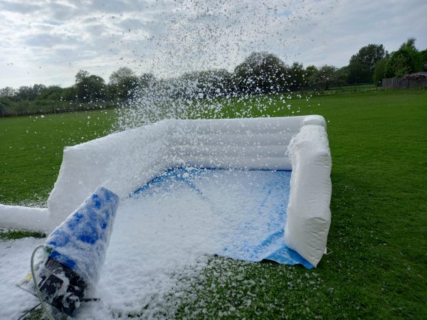 Inflatable foam cannon releasing foam in an outdoor setting on grass.