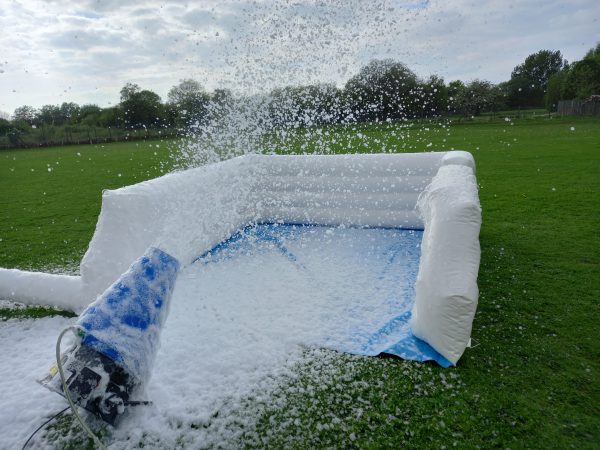 Inflatable foam cannon releasing foam in an outdoor setting on grass.