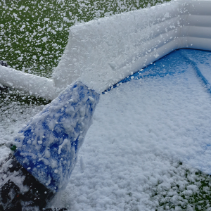 Foam cannon releasing a stream of foam in a party setting with an inflatable backdrop.