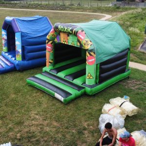 Two inflatable bounce houses in a grassy area, one blue and one green with various designs.