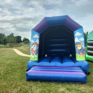 Paw Patrol themed bounce house featuring characters on the sides in a blue and purple design.