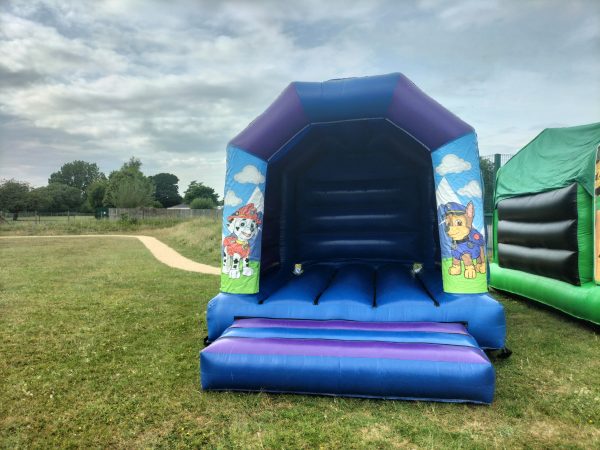 Paw Patrol themed bounce house featuring characters on the sides in a blue and purple design.
