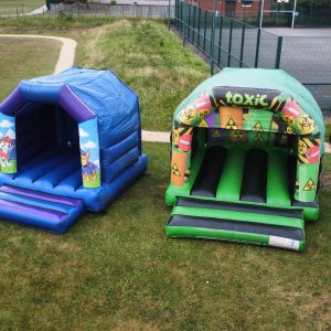 Two inflatable bouncy castles, one blue and one green, set up on a grassy area.