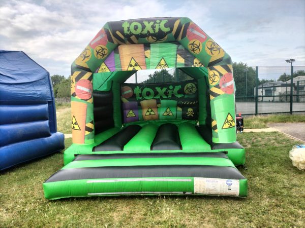 Inflatable bounce house with a toxic theme featuring hazard symbols and bright colors.