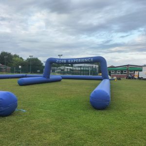 Large blue inflatable structure with the text 'Zorb Experience' on it set up on grass.