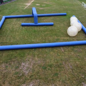 Aerial view of an inflatable obstacle course with blue barriers and large inflatable balls on grass.