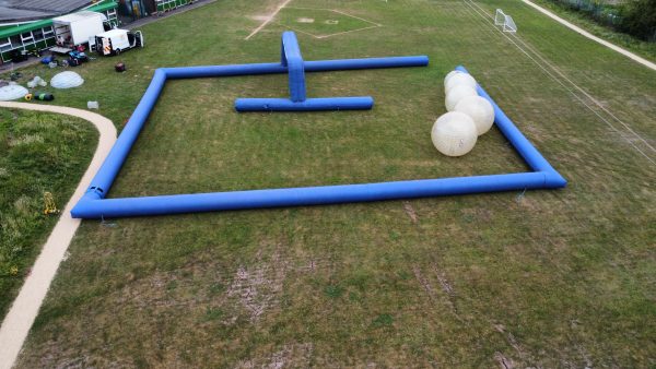 Aerial view of an inflatable obstacle course with blue barriers and large inflatable balls on grass.
