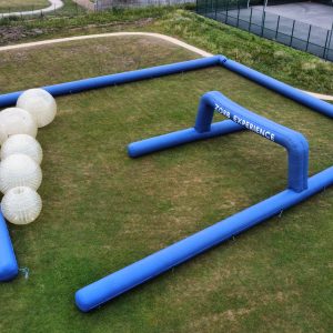 An inflatable Zorb ball arena with blue walls and white Zorb balls on the grass.