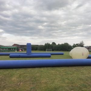 Inflatable obstacle course with blue barriers and a large white inflatable structure on grass.