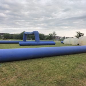 Inflatable obstacle course setup with blue barriers and transparent spheres on a grassy field.