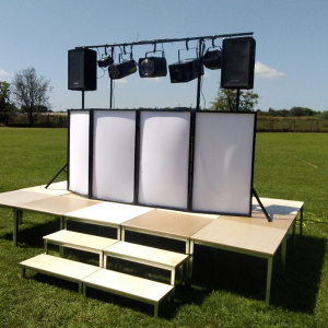 DJ set featuring speakers, lighting equipment, and a backdrop on a stage.