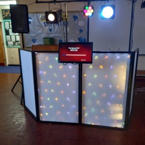 DJ set featuring a sound system, lighting, and a screen displaying a message.