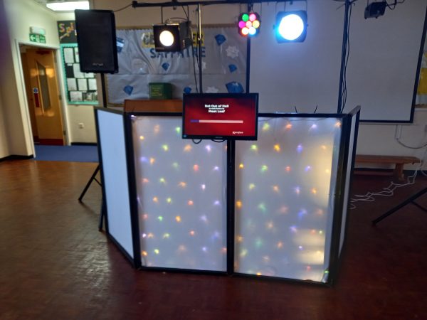 DJ set featuring a sound system, lighting, and a screen displaying a message.