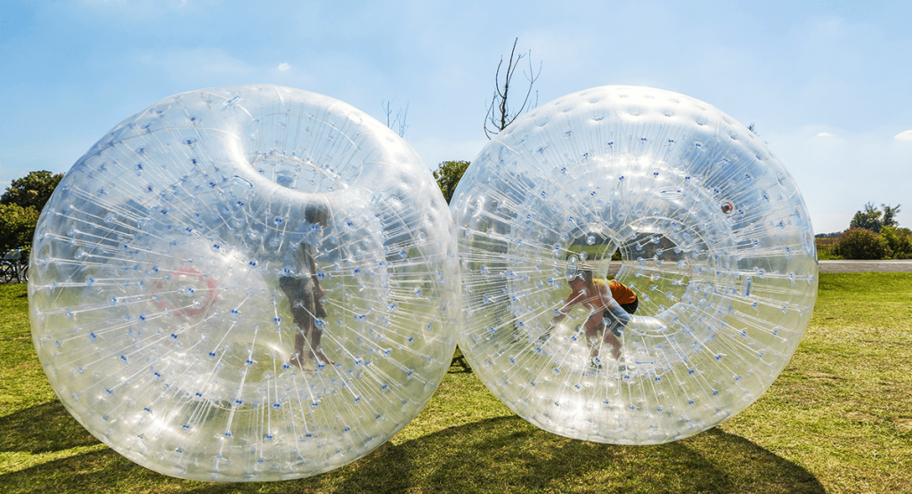 Two transparent inflatable zorbing balls with people inside on a grassy area.