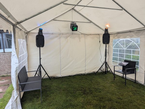 An indoor gazebo featuring two speakers, colored lights, and seating arrangements.